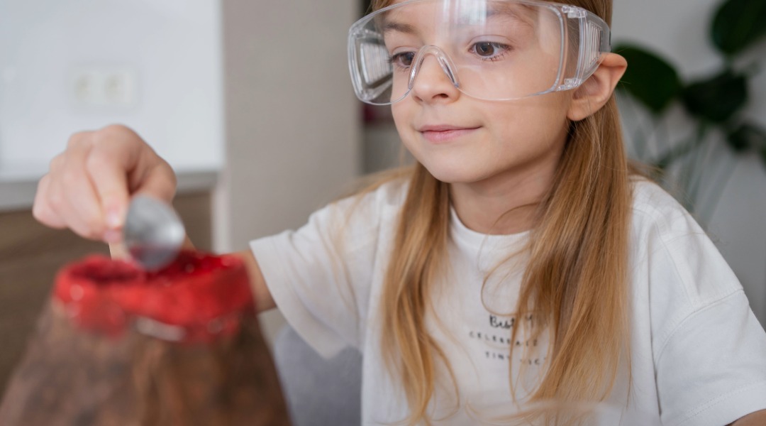 A picture of an 8 year old girl wearing experiment goggles doing a volcano science experiment.