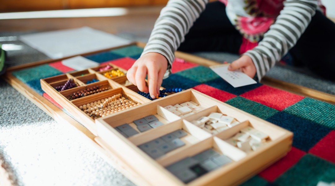 A child's hands working on the Montessori checker board, which helps children learn multiplication.