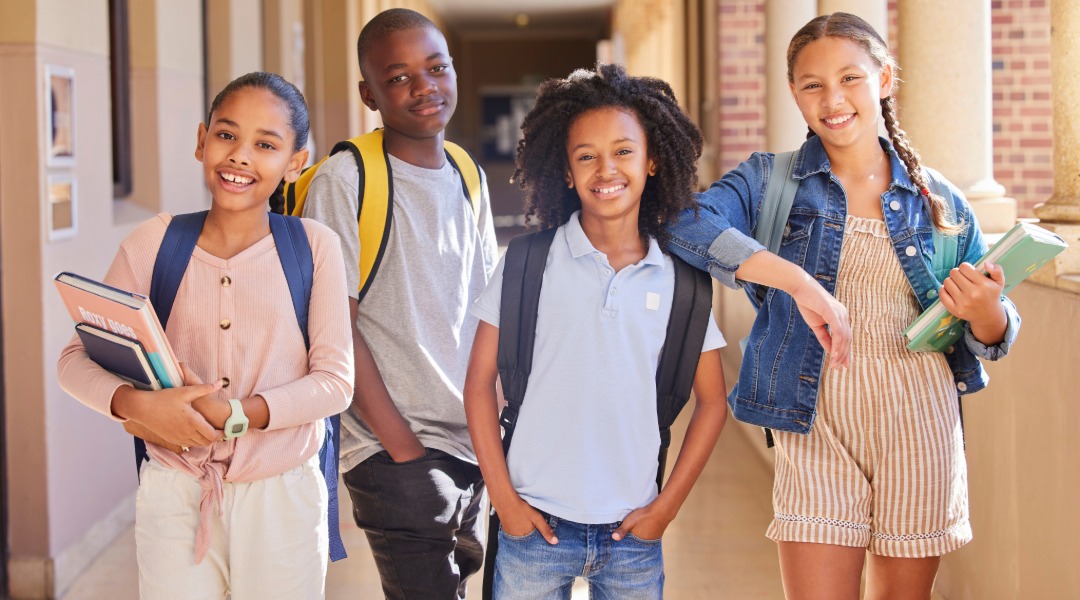 A group of 4 children smiling at the camera. Regardless, Montessori vs traditional school choose what fits best for your child.