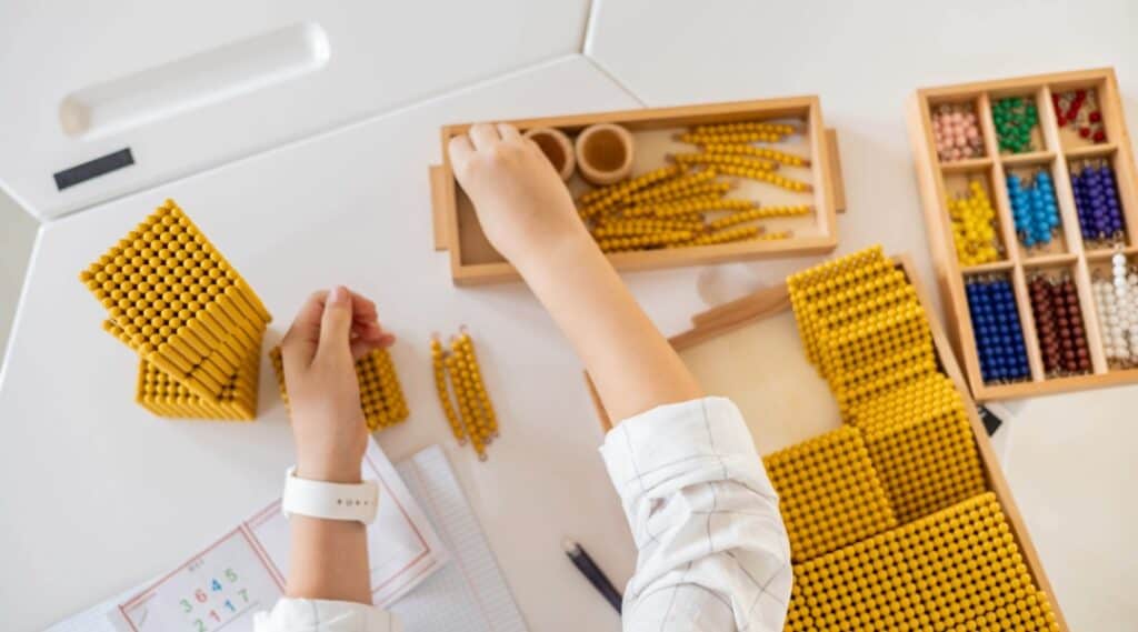 An image of the hands of an elementary Montessori student working with the golden bead math materials. A big difference between Montessori vs traditional school is the use of materials to learn concepts.
