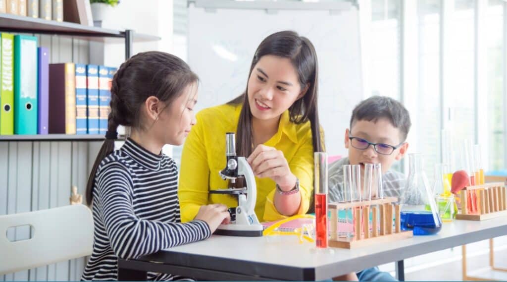 An elementary Montessori teacher guiding two students on how to use a microscope. 