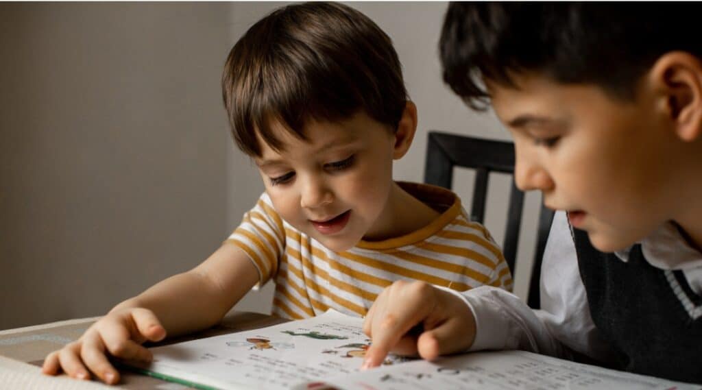 A 10 year old boy is helping a younger student with their reading.