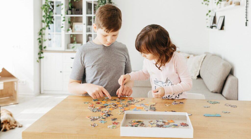 A young boy and his sister work together on a puzzle at home in a clean and organized space. This is how you can bring the Montessori prepared environment to your home.