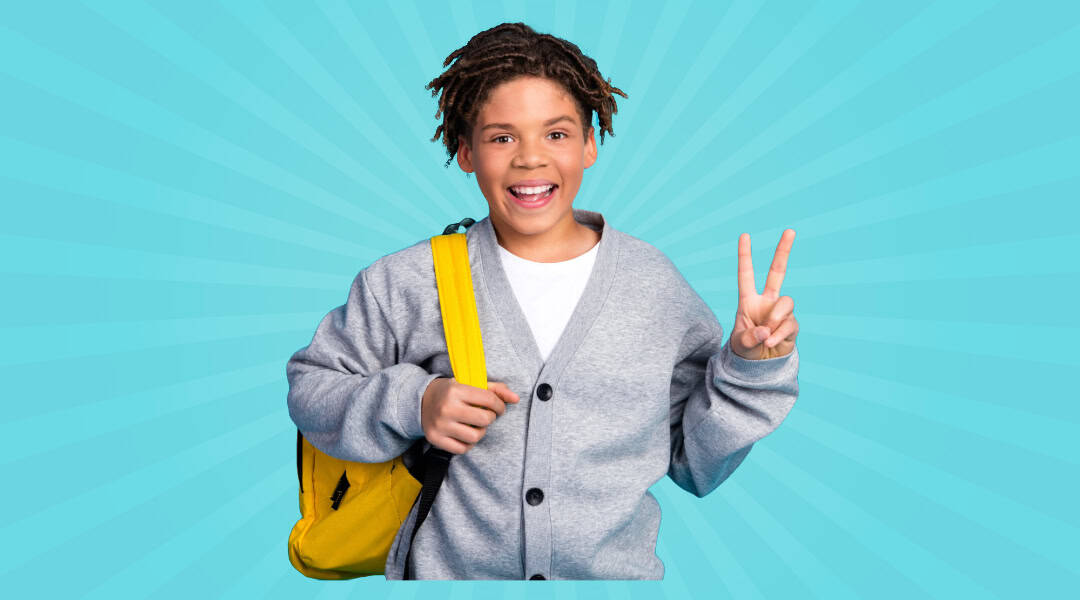 An upper elementary student wearing a yellow backpack smiling and giving the peace sign with his fingers.