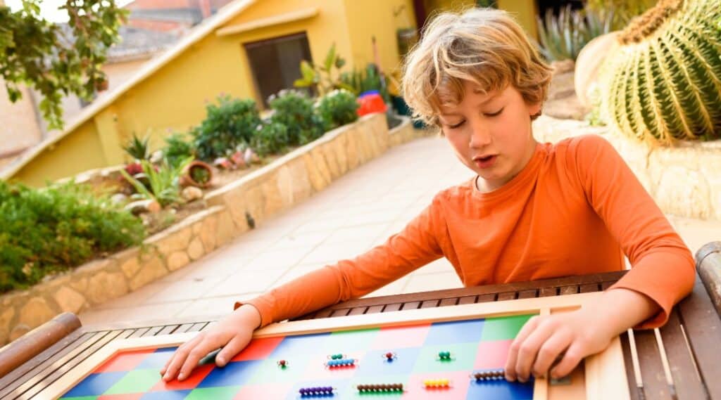A young boy using the Montessori checkerboard  outside to learn about multiplication.