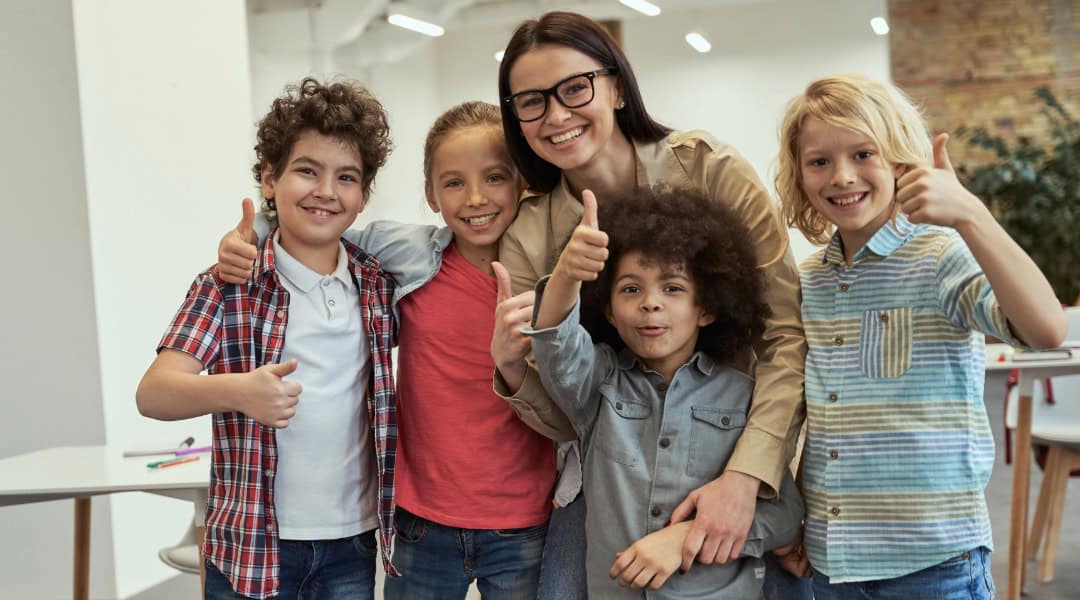 A teacher and four of her students smiling and giving thumbs up.