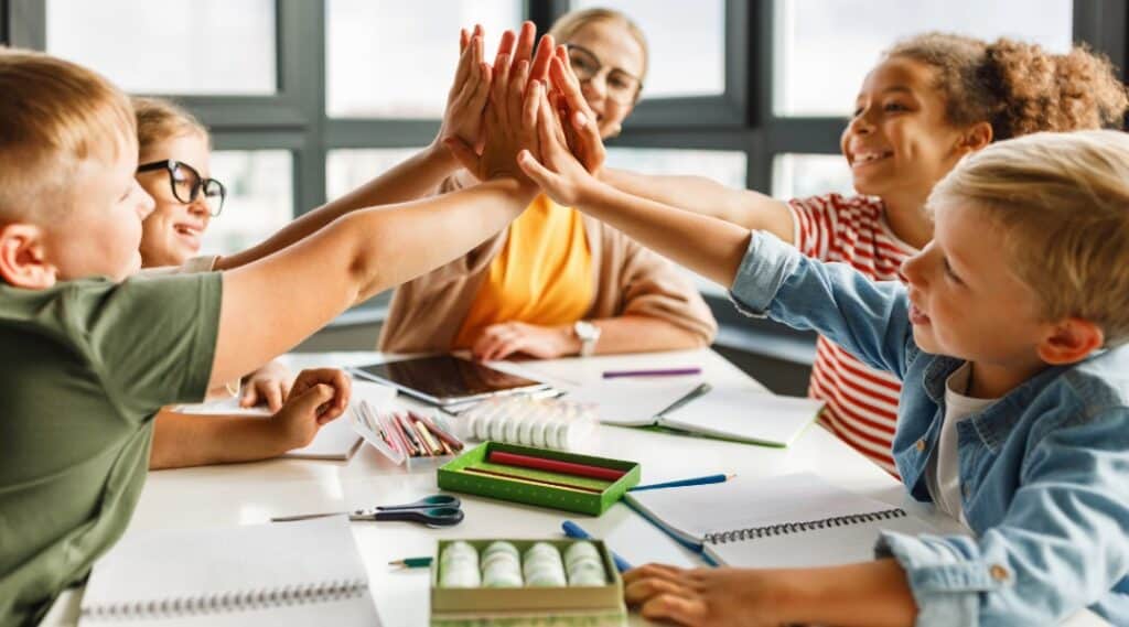 Happy, small group of students sitting at a table using games in the classroom giving each other high fives.