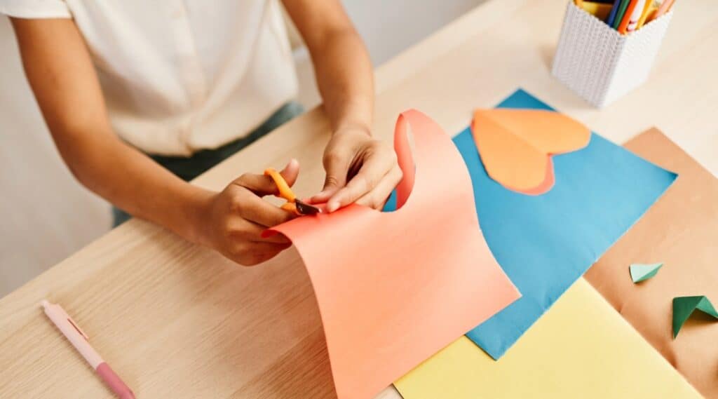 A young girl cutting out colored paper for her net of a cube printable.