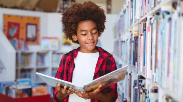 A 5th grade boy in the library looking at a picture book.