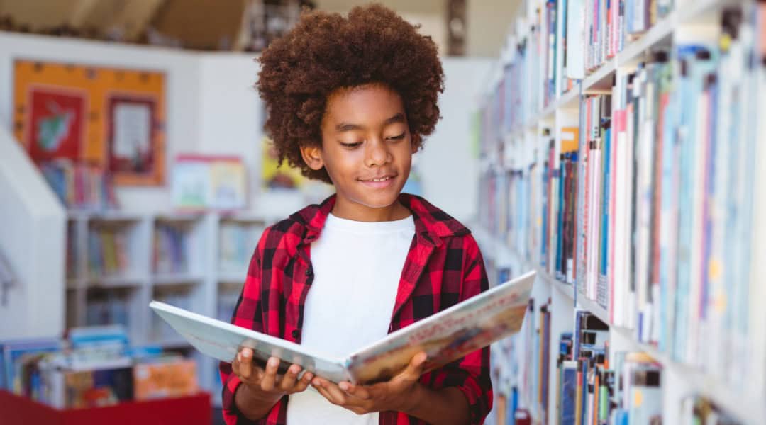 A 5th grade boy in the library looking at a picture book.