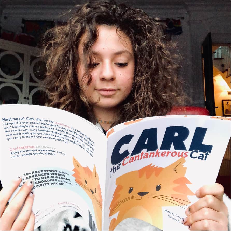 Image of a young girl with curly hair reading a copy of Carl the Cantankerous Cat which is a great picture book for 5th graders.