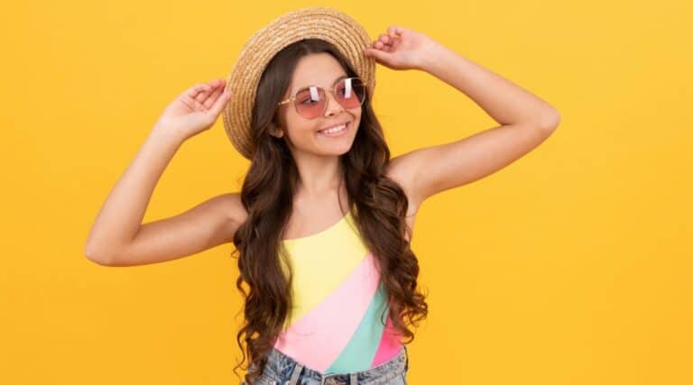 A 12 year old girl in a sun hat and sunglasses wearing a swimsuit with jean shorts over top. She is hoping to avoid the summer brain drain!