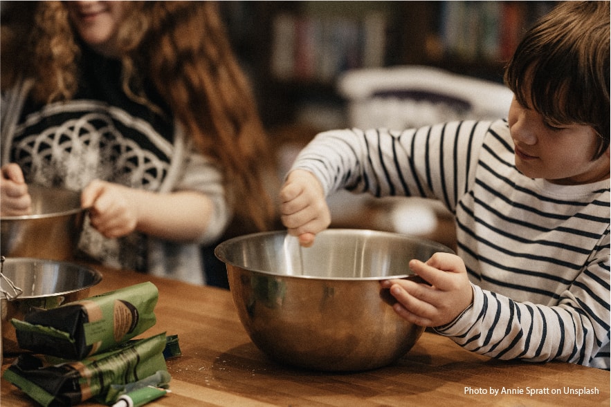 A picture of a boy and a girl in the kitchen mixing ingredients in a bowl. They are having fun learning while they improve their reading skills by reading a recipe.