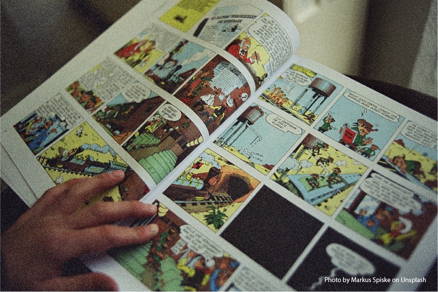 A picture of a comic book open and being read. A small hand is shown on the lower left page. Comic books are one of many awesome summer reading activities elementary kids will love!