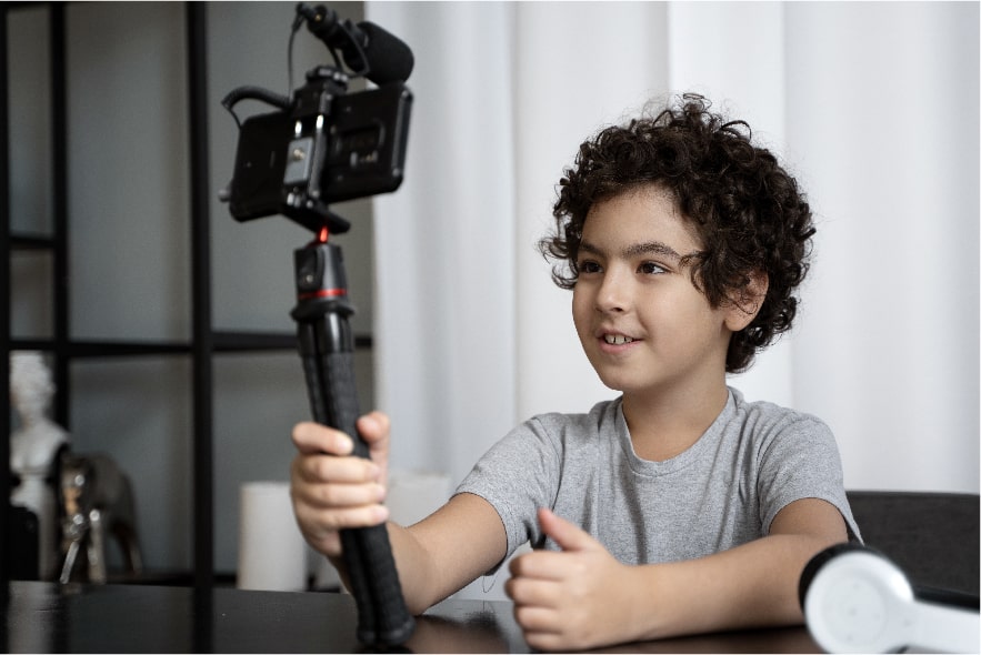 A picture of a 9 year old boy holding a camera arm and facing the camera at himself to film his book report trailer. 