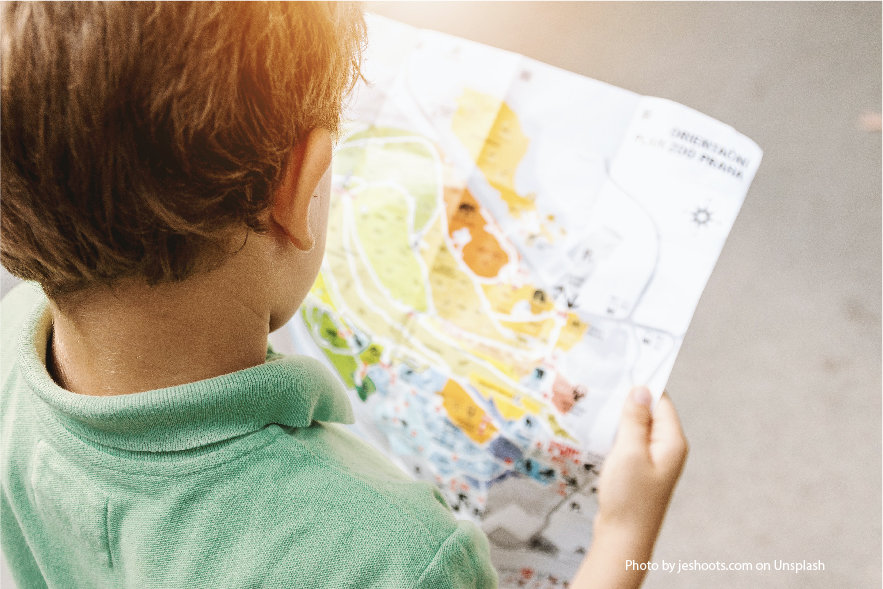 A picture over the shoulder of a young boy who is reading an amusement park map. It is important to encourage kids to read everything. 