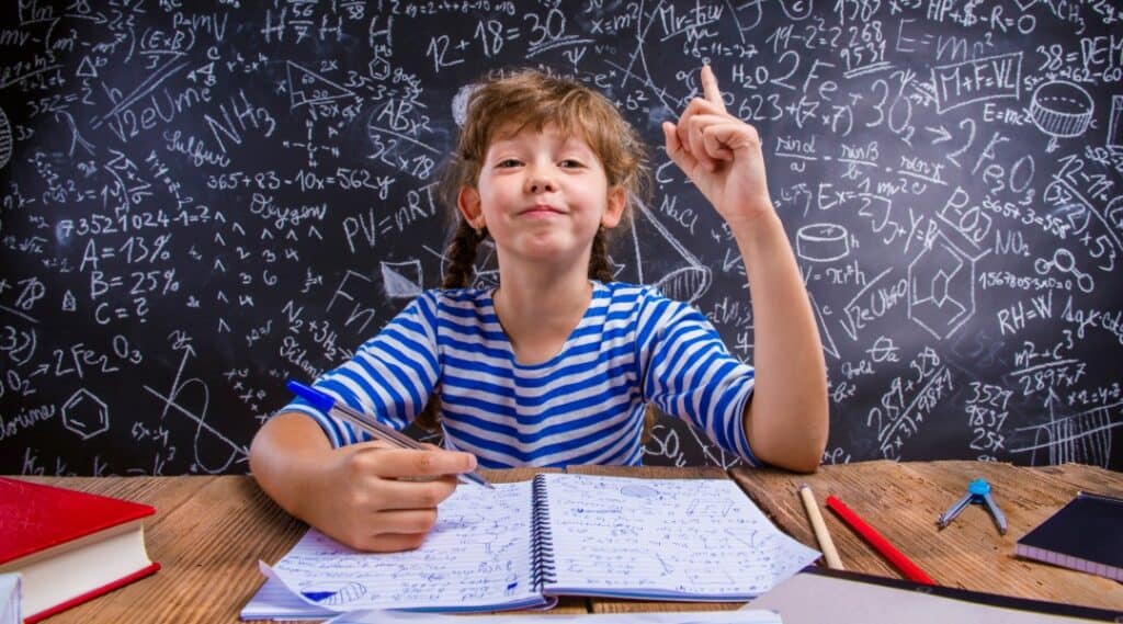 A 12 year old girl sitting in front of a chalkboard and ready to solve some Montessori command card questions.
