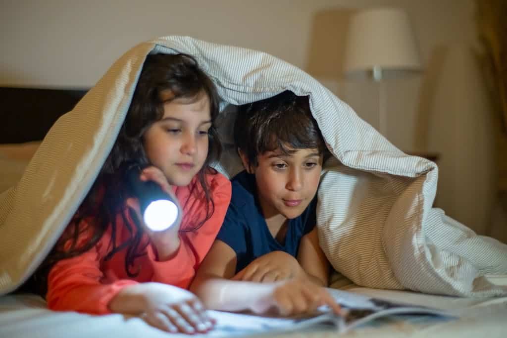 A Boy and a Girl Under a Blanket Reading a Book