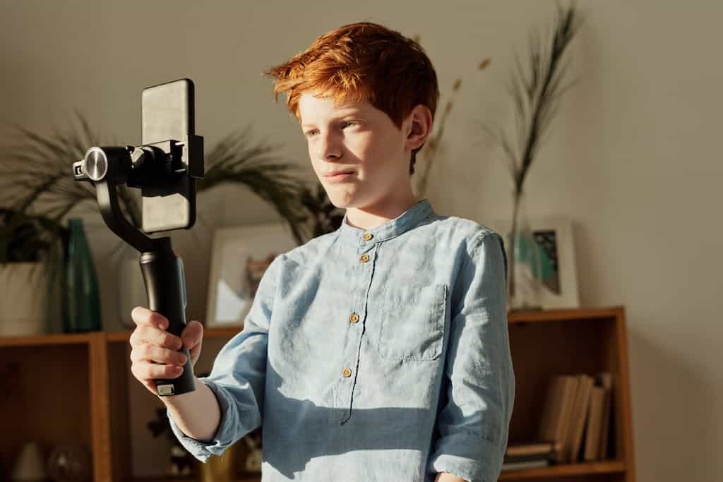 Boy in Blue Dress Shirt Holding Black Selfie Stick recoding himself for a. movie trailer for the book he read. This is a popular book report ideas for 5th grade.