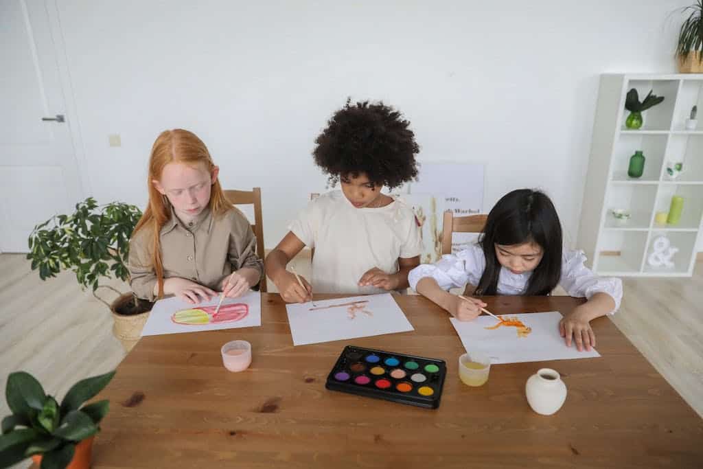 From above of attentive diverse elementary girls sitting at table and working on their book report ideas for 5th grade.