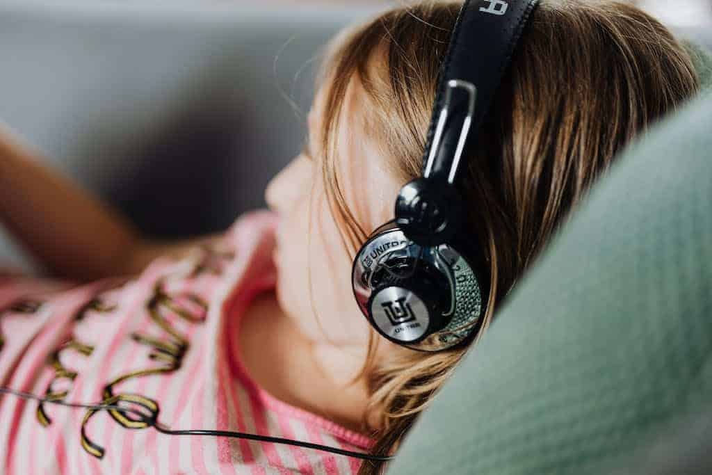 Girl in Modern Headphones Listening to an audiobook in her classroom.