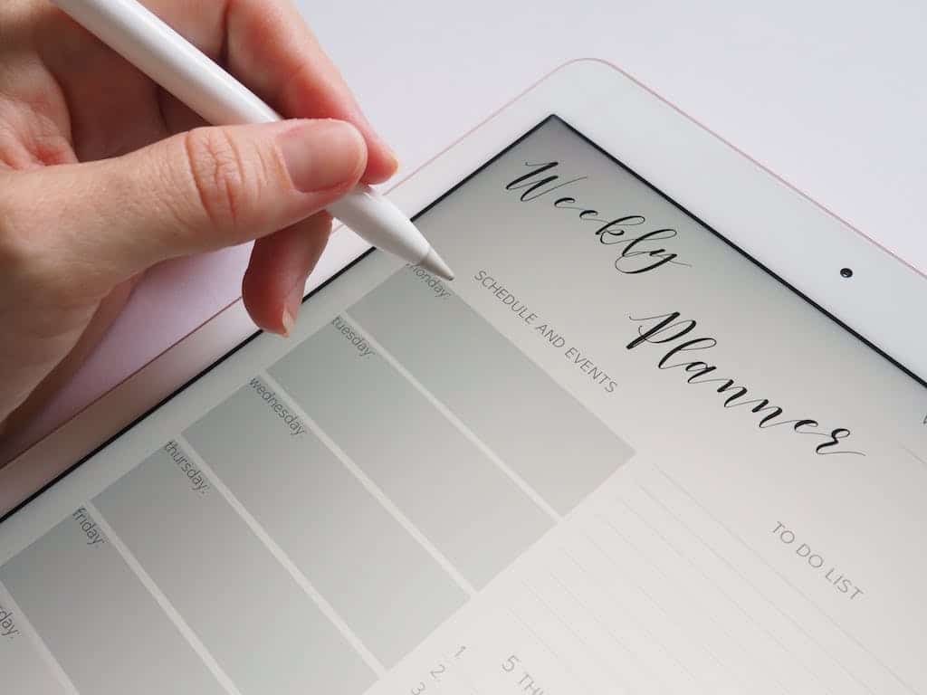 Person Holding White Stylus about to pencil in the date for family book club.