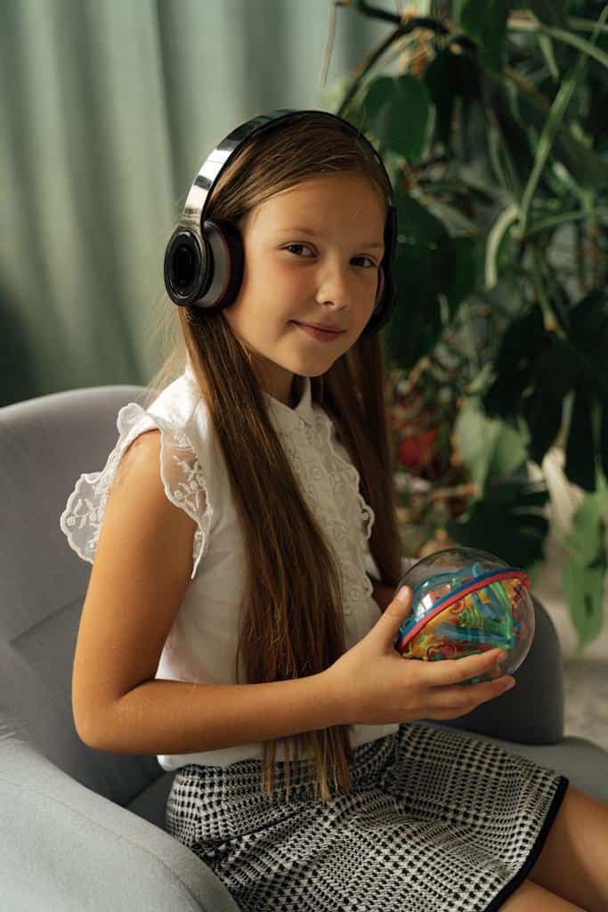 Grade 5 girl in White cap sleeve Dress Wearing Black Headphones listening to an audiobook in the classroom.