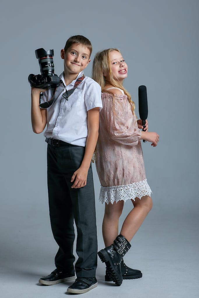 A Boy Holding a Camera Beside a Girl Holding Microphone ready to do an interview as their book report assignment. This is one of our favourite book report ideas for 5th grade.