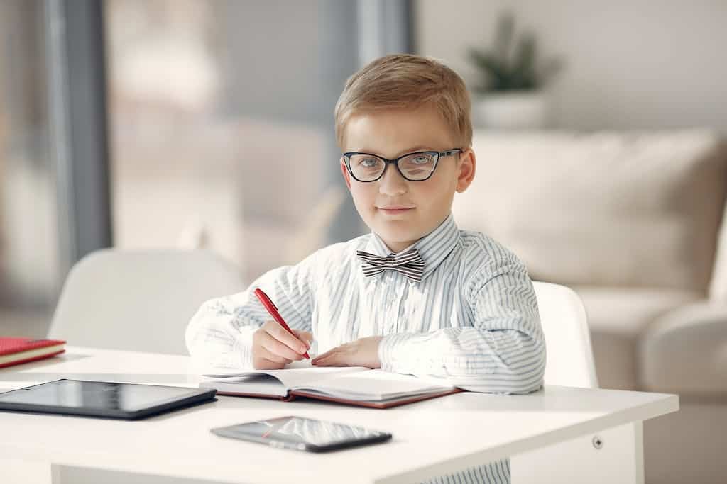 Boy in Black and White Striped Dress Shirt Wearing Eyeglasses writing a to do list as his book report for 5th grade.