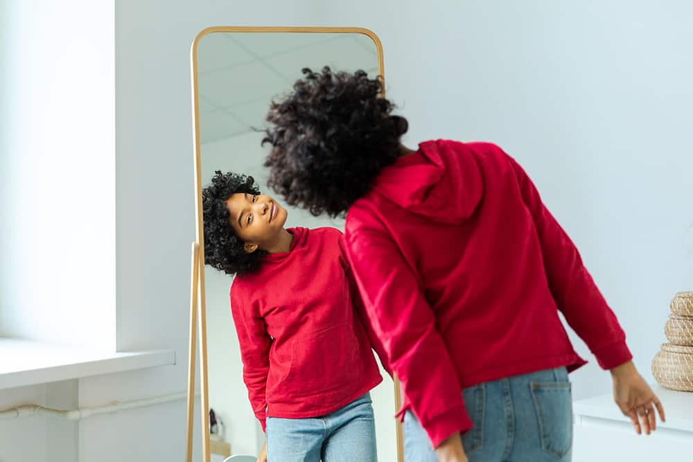 Young smiling African American girl looking into a full length mirror enjoying her reflection. 