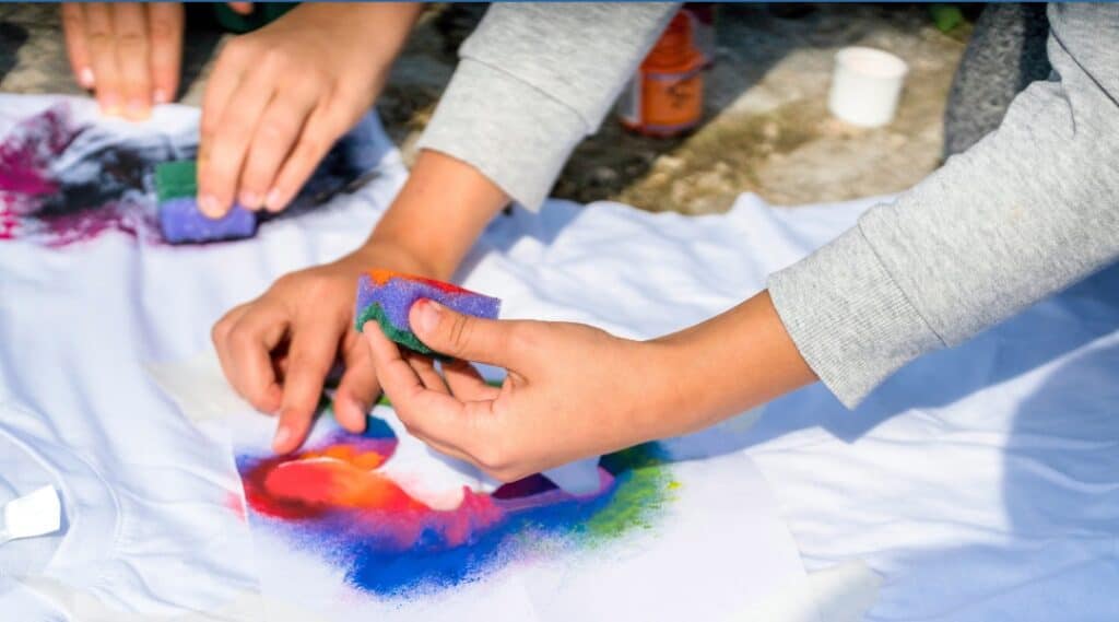 A picture of a child's hands holding a sponge with paint. They are making a tshirt original.