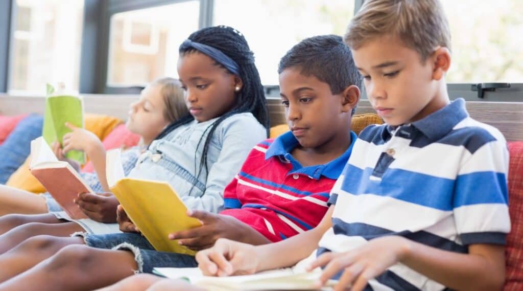 Four elementary students sitting reading books.