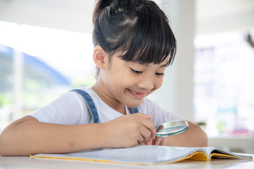 Asian Little girl reading the books on the desk with a magnifying glass
