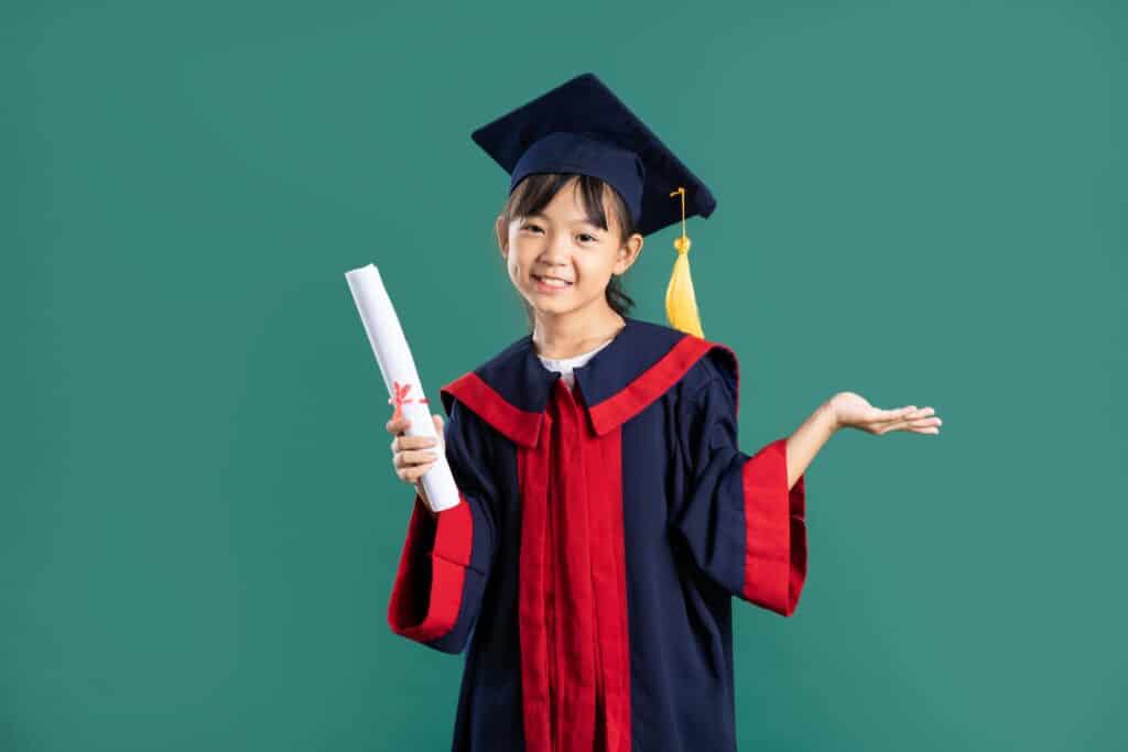 A grade 6 Asian girl dressed in a graduation cap and gown holding a diploma.