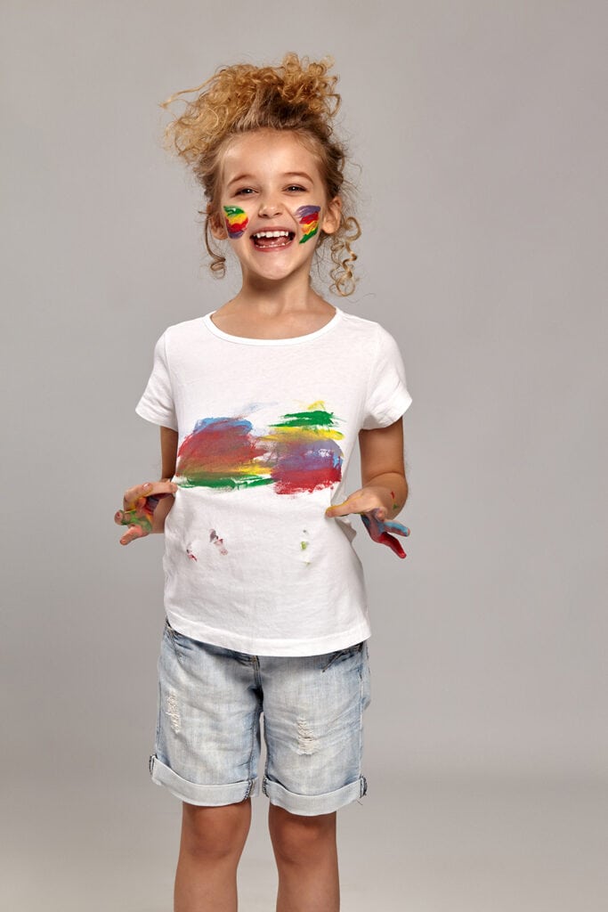 Elementary-aged girl wearing a white t-shirt that she smeared paint on. This is her book report representing what the main character would wear. 