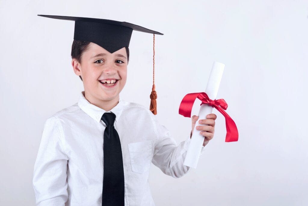 Grade 6 boy with a graduation cap on holding a graduation certificate. Smiling because he loves elementary graduation quotes.