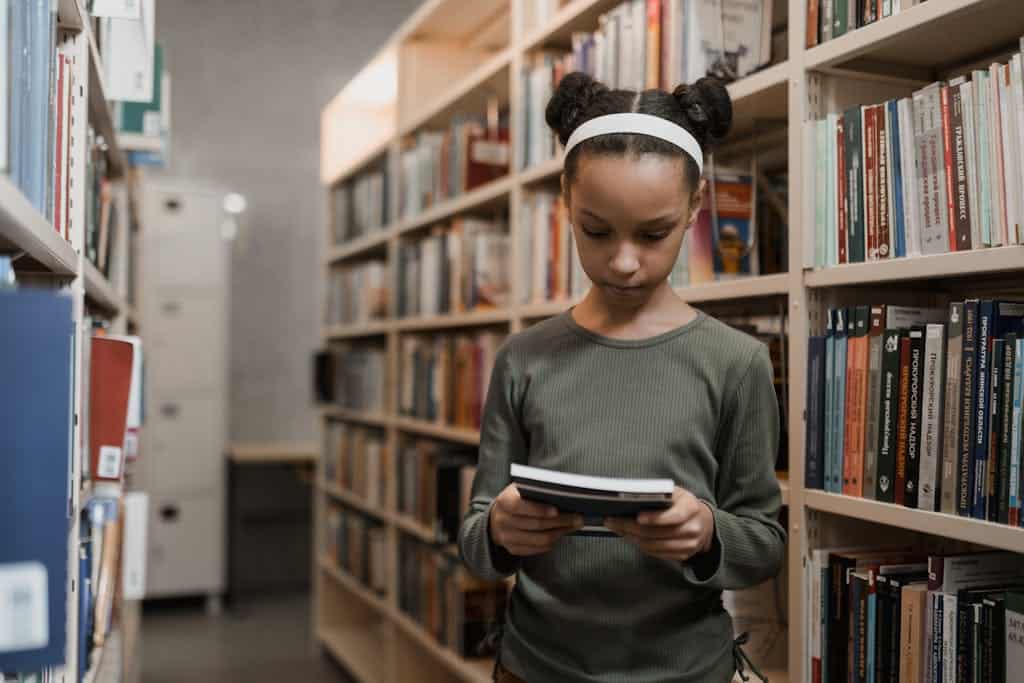 Young Girl Looking at a Book while doing a library scavenger hunt