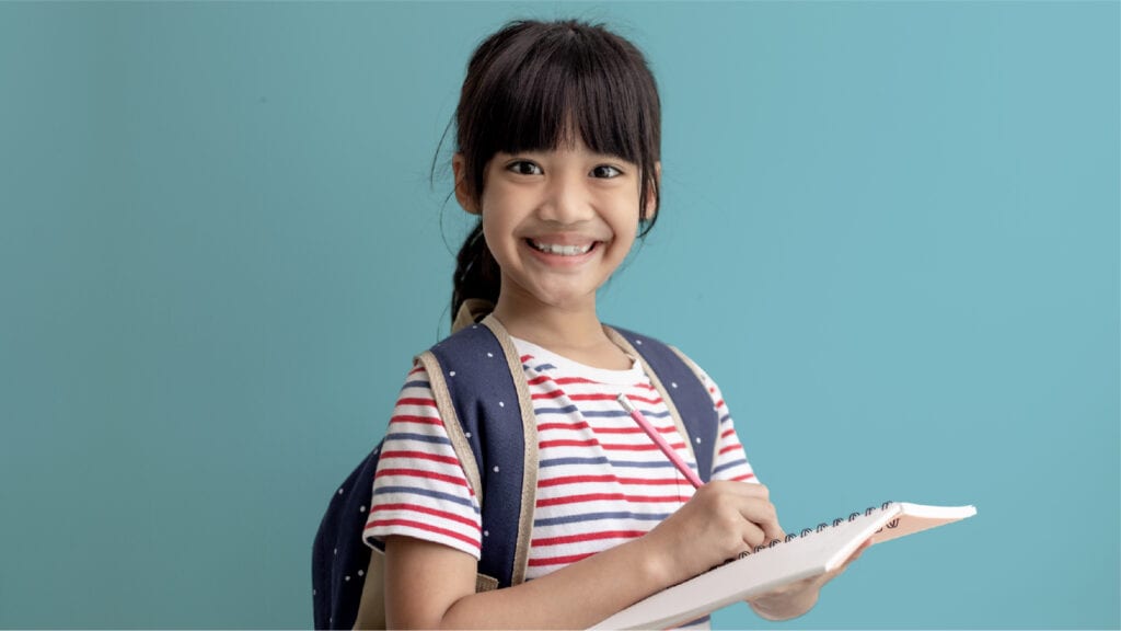 An image of a 10-year old  girl with a backpack on holding a notebook. She's doing a scavenger hunt.