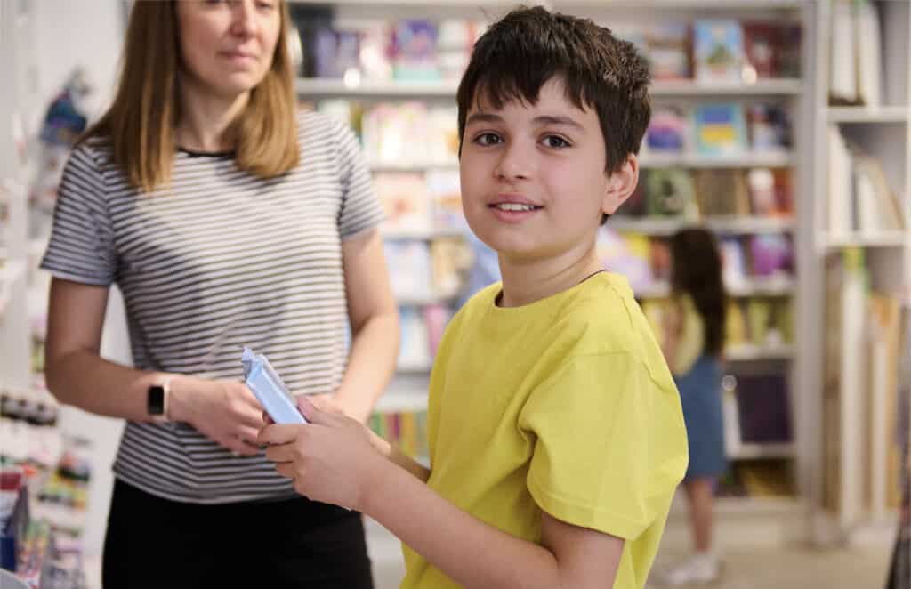 A 9-year-old boy in a yellow t-shirt asking his teacher for book recommendations.