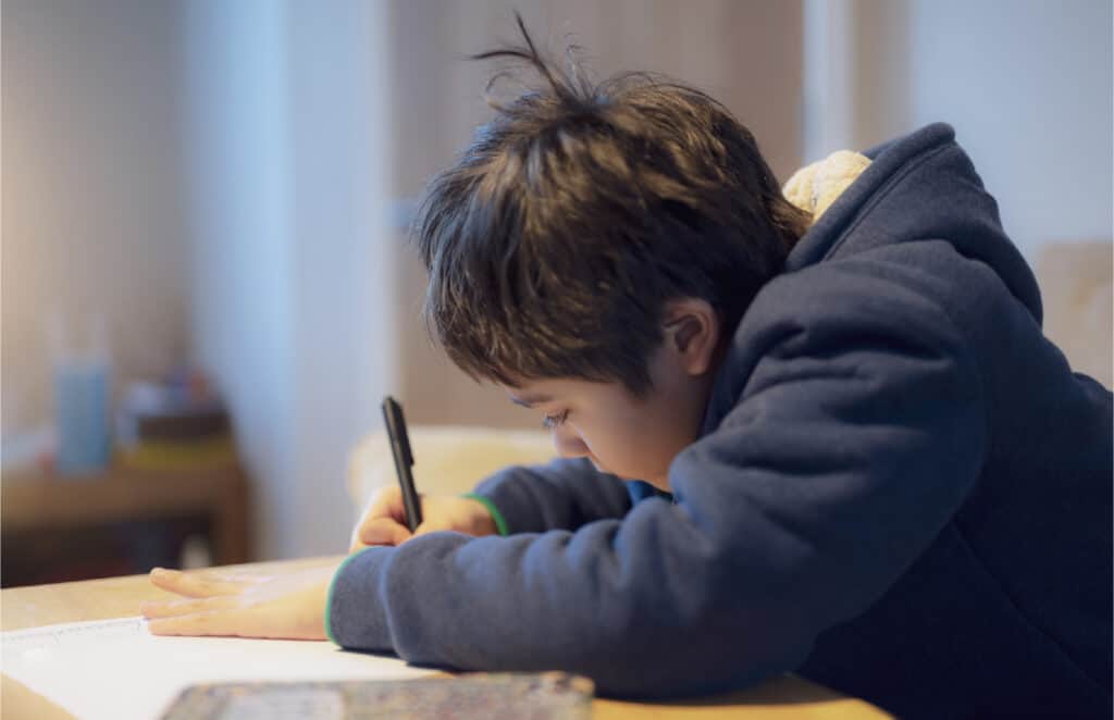 An image of an 8 year old boy sitting at a table writing a story.