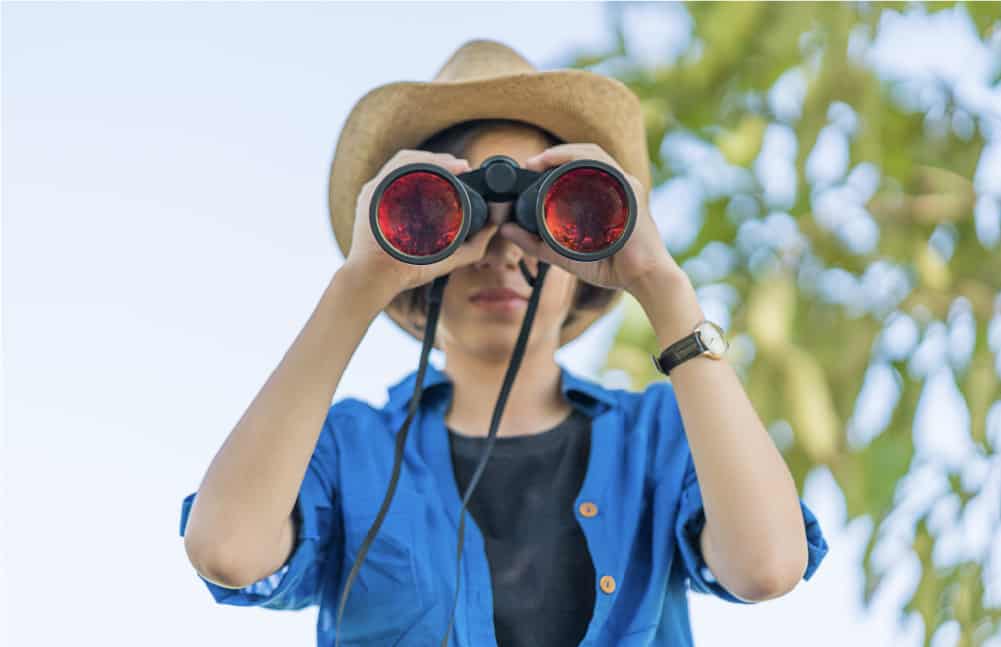 An image of an elementary-aged child looking through binoculars. They are looking for reading materials for their library scavenger hunt.