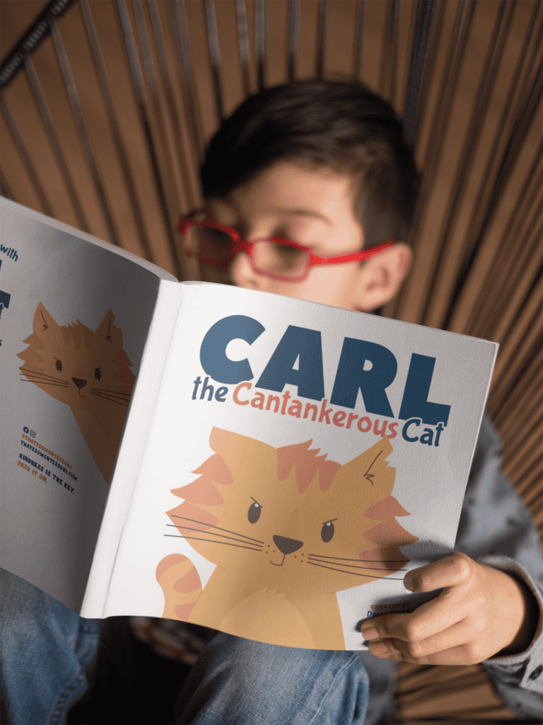 An 8 year old boy with red glasses sitting reading one of the best picture books to teach vocabulary, Carl the Cantankerous Cat.