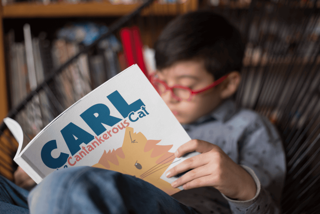 A 10 year old boy with red glasses reading Carl the Cantankerous Cat.