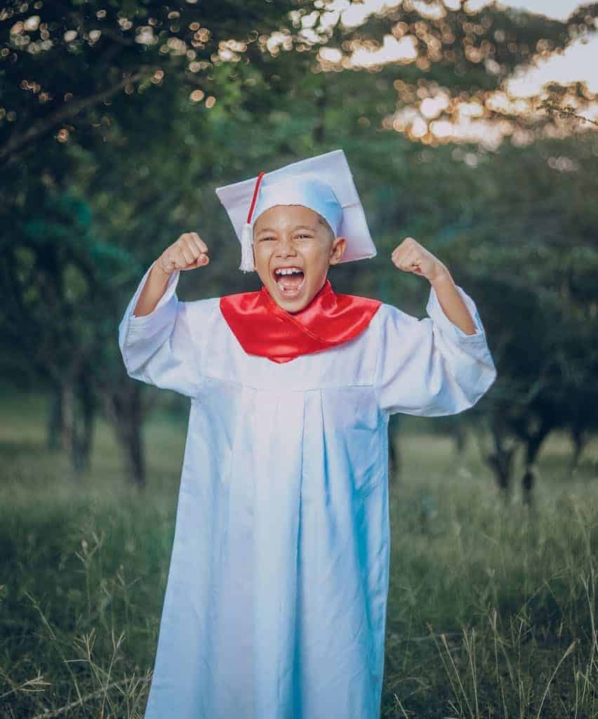 Small Boy in White Robe and Mortarboard Hat Celebrating elementary Graduation