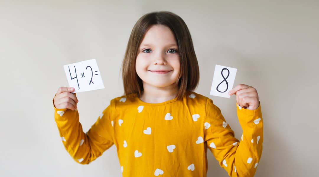 A young elementary student holding math flash cards, a fun and educational way to learn math facts.