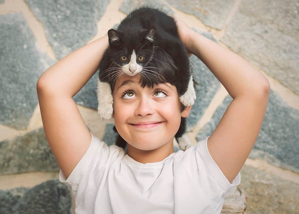 Happy child holding a black and white cat on their head.