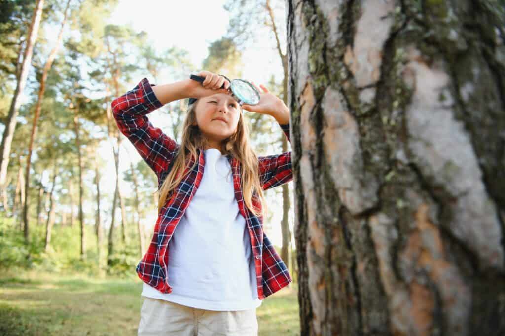 Image of an elementary student with a magnifying glass exploring the nature outdoors while she does an alphabet scavenger hunt.