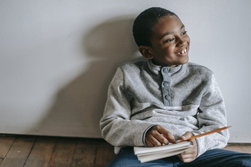 Happy African American boy sitting on floor with copybook and pencil reflecting on the short quotes for students he read.