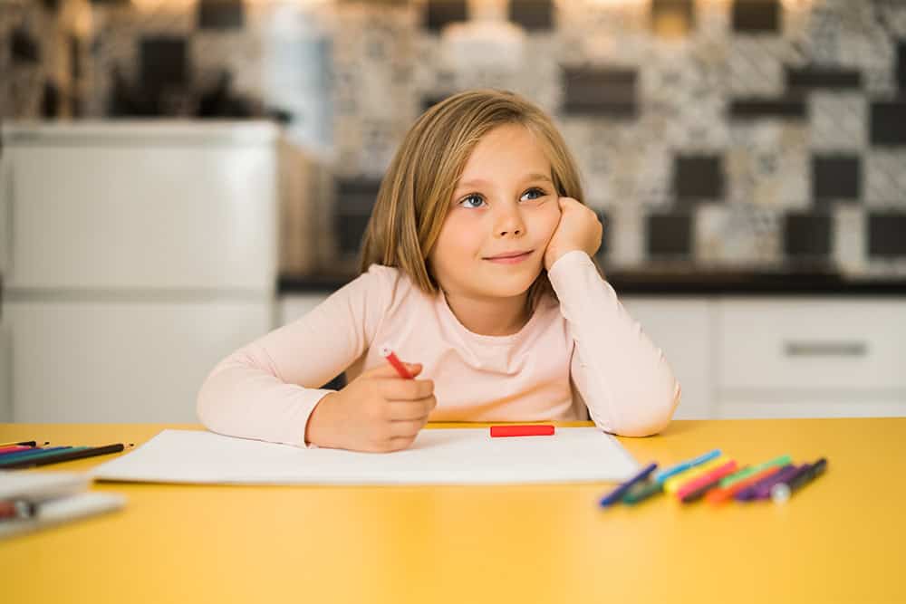 A young girl sitting at a desk holding a crayon. She is going to write a short quote for students to be inspired by.