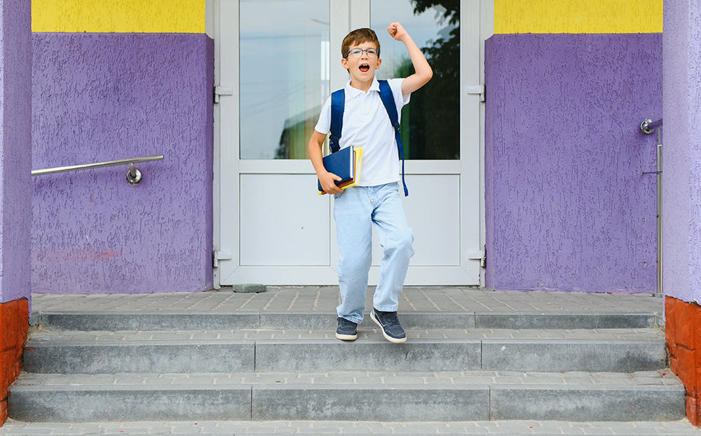 Picture of a young boy going to school. He's excited and holding some books in his right hand.